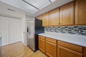 Kitchen with stainless steel fridge with ice dispenser, light wood-type flooring, light countertops, backsplash, and brown cabinetry