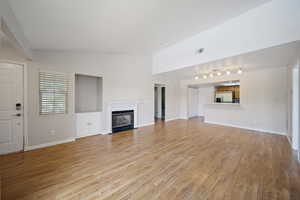 Unfurnished living room featuring a glass covered fireplace, vaulted ceiling, light wood-type flooring, and rail lighting