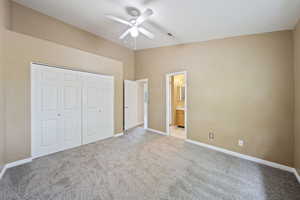 Unfurnished bedroom featuring light colored carpet, a closet, lofted ceiling, ceiling fan, and ensuite bathroom