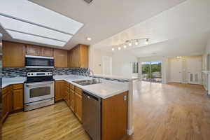 Kitchen featuring stainless steel appliances, light countertops, a peninsula, open floor plan, and light wood-style flooring