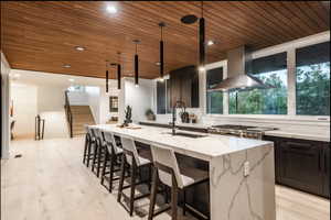 Kitchen featuring range hood, wood ceiling, healthy amount of natural light, a kitchen island with sink, and light stone countertops