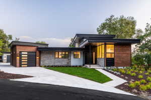 Modern home with a garage, driveway, stone siding, and a front lawn
