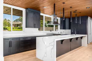 Kitchen with wood ceiling, wall chimney exhaust hood, healthy amount of natural light, light stone counters, and recessed lighting