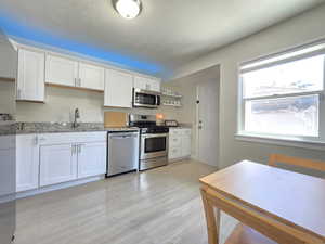 Kitchen with stainless steel appliances, light stone countertops, white cabinets, light wood-style floors, and open shelves