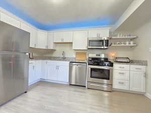 Kitchen with appliances with stainless steel finishes, light wood-type flooring, white cabinetry, and light stone counters