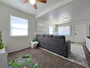 Carpeted living room featuring plenty of natural light, ceiling fan, and beamed ceiling