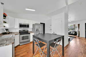 Kitchen with appliances with stainless steel finishes, vaulted ceiling, open shelves, light wood-type flooring, and white cabinets
