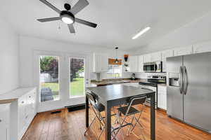 Kitchen featuring stainless steel appliances, white cabinetry, vaulted ceiling, light wood finished floors, and plenty of natural light
