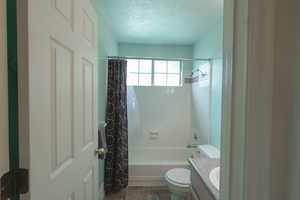 Full bath featuring a textured ceiling, vanity, and shower / bath combo with shower curtain