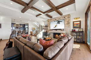 Living room with wood-type flooring, stairway, a stone fireplace, coffered ceiling, and beamed ceiling