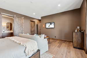 Bedroom featuring a barn door, light wood-style flooring, connected bathroom, and recessed lighting