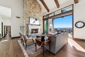 Living area with a high ceiling, beamed ceiling, hardwood / wood-style flooring, and a stone fireplace
