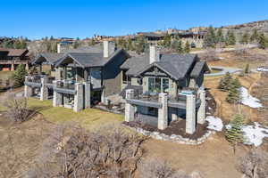 Rear view of property with a chimney, stone siding, a wooden deck, a balcony, and a patio