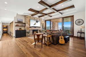 Living room with light wood finished floors, beam ceiling, coffered ceiling, a stone fireplace, and recessed lighting