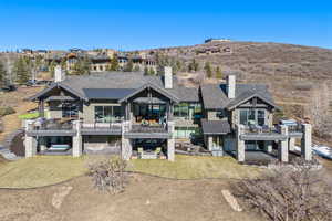 Back of property featuring a chimney, a balcony, stone siding, and an outdoor hot tub