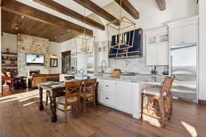 Kitchen with built in fridge, a chandelier, backsplash, a large fireplace, and white cabinets