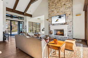 Living area with high vaulted ceiling, a stone fireplace, beam ceiling, and wood finished floors