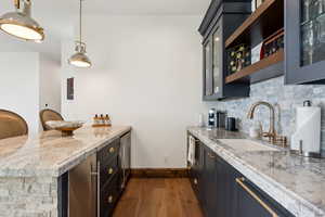 Kitchen with dark wood finished floors, tasteful backsplash, light stone counters, beverage cooler, and a peninsula