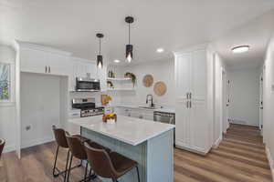 Kitchen featuring appliances with stainless steel finishes, open shelves, white cabinets, wood finished floors, and recessed lighting