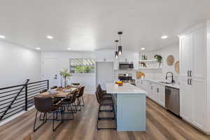 Kitchen with stainless steel appliances, open shelves, wood finished floors, light countertops, and recessed lighting