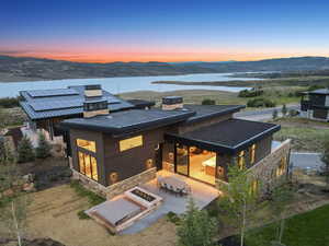 Back of property at dusk with stone siding, a chimney, a patio, outdoor dining space, and solar panels