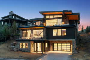 View of front of property featuring a balcony, concrete driveway, stone siding, and a garage