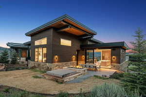 Back of house at dusk with stone siding, a patio, and an outdoor fire pit