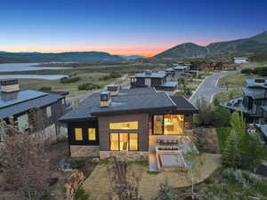 Back of house at dusk featuring a mountain view, stone siding, a patio, and a chimney