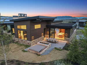 Back of property at dusk with stone siding, a patio area, and a fire pit