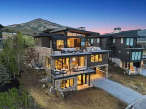 Back of property with stone siding, a patio area, driveway, and a balcony