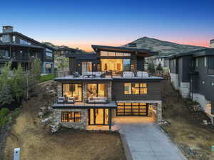 Back of property at dusk with a balcony, driveway, stone siding, and an attached garage