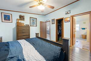 Bedroom with wood finished floors, a spacious closet, crown molding, a closet, and connected bathroom