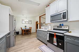 Kitchen with appliances with stainless steel finishes, gray cabinets, light countertops, and light wood-style floors