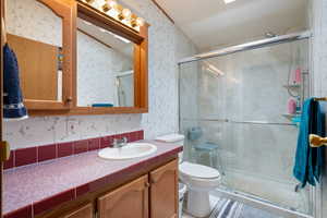 Full bath featuring wallpapered walls, vanity, and a stall shower