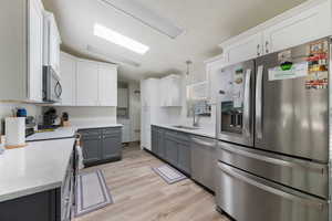 Kitchen featuring appliances with stainless steel finishes, light wood-type flooring, a textured ceiling, and white cabinets