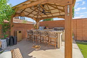 Fenced backyard featuring a gazebo, exterior kitchen, ceiling fan, and a patio area