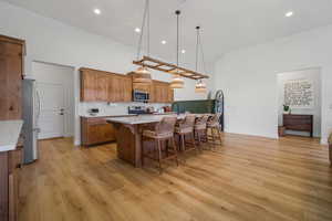 Kitchen with appliances with stainless steel finishes, light countertops, brown cabinetry, high vaulted ceiling, and light wood-style floors