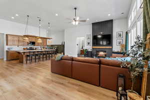 Living room with ceiling fan, recessed lighting, a large fireplace, light wood-style flooring, and a towering ceiling