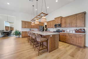 Kitchen featuring stainless steel appliances, a kitchen island with sink, a towering ceiling, a breakfast bar, and backsplash