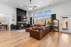 Living room with a fireplace, ceiling fan, light wood-style flooring, a towering ceiling, and recessed lighting