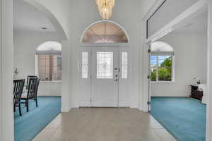 Foyer with light colored carpet, a chandelier, arched walkways, light tile patterned floors, and crown molding