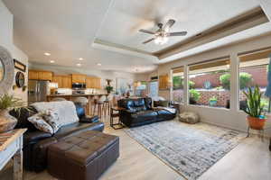 Living area featuring a ceiling fan, a tray ceiling, light wood-style floors, and recessed lighting