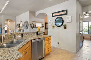 Kitchen with stainless steel dishwasher, arched walkways, ceiling fan, and light tile patterned floors