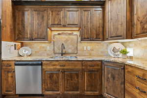Kitchen featuring dishwasher, decorative backsplash, and light stone counters