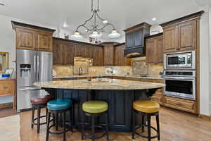 Kitchen with appliances with stainless steel finishes, light stone countertops, a kitchen island, light wood finished floors, and decorative backsplash