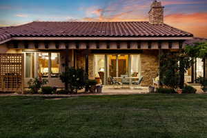 Rear view of house featuring stone siding, a tiled roof, a patio, and a yard