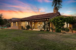 Back of property at dusk with a chimney, a patio, a lawn, a tile roof, and stucco siding