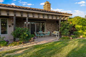 Back of house with stone siding, a yard, a chimney, stucco siding, and a patio