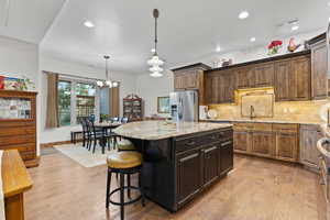 Kitchen featuring stainless steel fridge, light wood finished floors, light stone countertops, backsplash, and a chandelier
