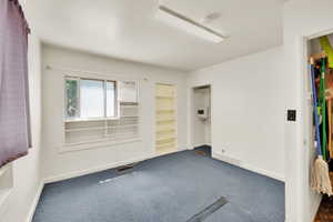 Empty room featuring a smoke detector, dark colored carpet, and cooling unit
